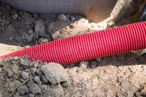 Workers lay down a red plastic drainage pipe in the brown soil, preparing for Stock-Fotos