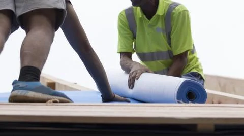 Workers lay an insulating layer of non-woven fabric on the roof. Stock Photos