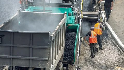 Workers lay a new asphalt coating using hot bitumen. Work of heavy machinery  Stock Photos
