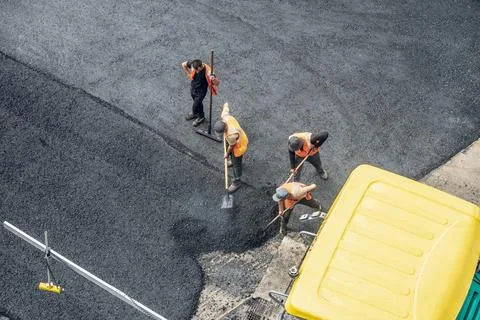 Workers lay a new asphalt coating using hot bitumen. Work of heavy machiner.. Stock Photos