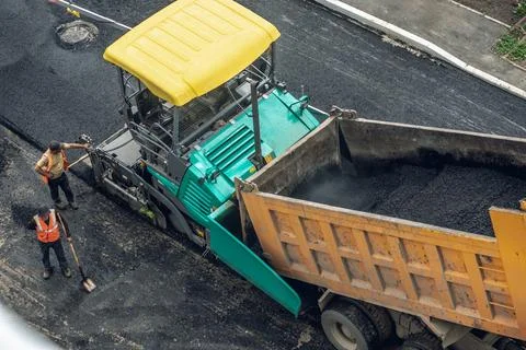 Workers lay a new asphalt coating using hot bitumen. Work of heavy machiner.. Stock Photos