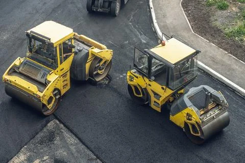 Workers lay a new asphalt coating using hot bitumen. Work of heavy machinery  Stock Photos