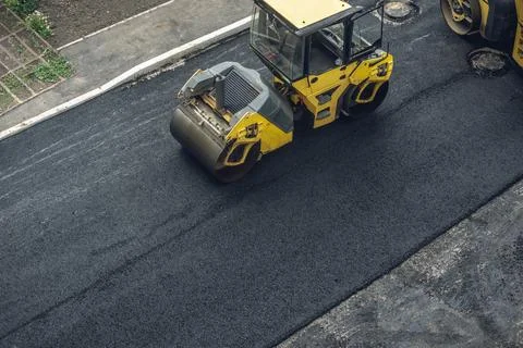 Workers lay a new asphalt coating using hot bitumen. Work of heavy machinery  Stock Photos