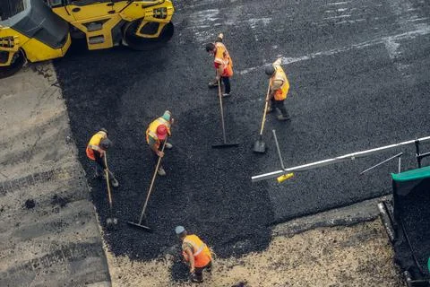 Workers lay a new asphalt coating using hot bitumen. Work of heavy machinery  Stock Photos