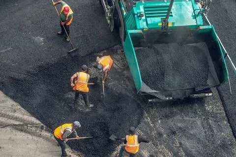 Workers lay a new asphalt coating using hot bitumen. Work of heavy machinery  Stock Photos