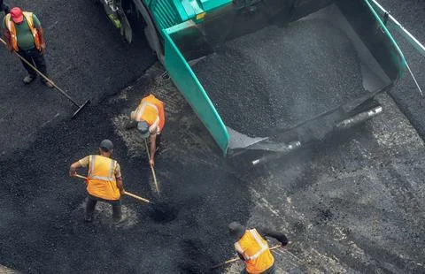 Workers lay a new asphalt coating using hot bitumen. Work of heavy machinery  Stock Photos