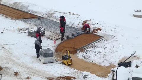 Workers lay pavement in snowy conditions at construction site during winter Stock Footage 328426314