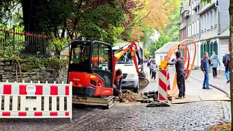 Workers laying cable using mini excavator on cobbled street in Monschau Stock Footage 348315881