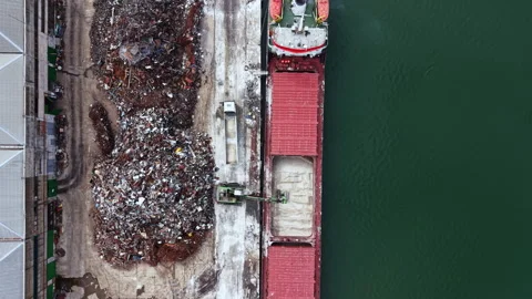 Workers load cargo onto a ship at a busy port near a large pile of scrap metal Stock Footage 337906652