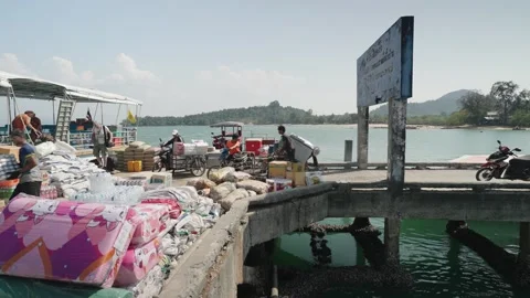 Workers load goods and supplies at a riverside pier with boats in Ranong Stock Footage 327721988