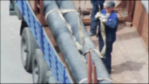 Workers loading large industrial pipes onto a flatbed truck using lifting straps Stock Footage 344864185