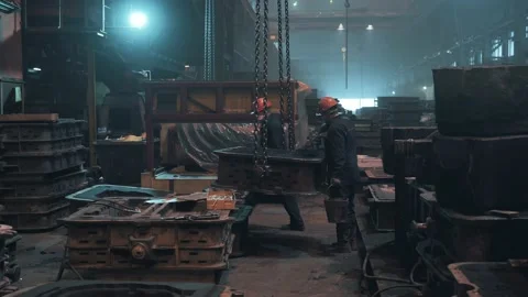 Workers in masks and helmets take cargo on chains from load crane in workshop of Stock Footage 153117010