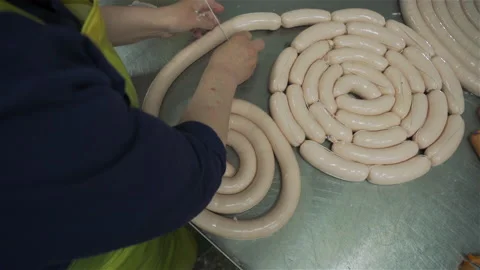 Workers in meat factory forming many short sausages from one long sausage. Sausa Stockbeeldmateriaal 131868871