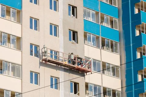 Workers on a mobile platform are plastering the windows of the house with Stock Photos