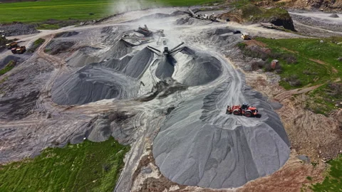 Workers operate machinery at a granite quarry during the day with piles of Stock Footage 340167383