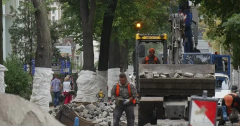 Workers in Orange Workwear Are Working at Road Repair Yellow Excavator with Stock Footage 54334518