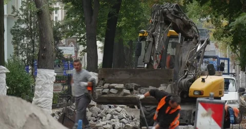 Workers in Orange Workwear Are Working at Road Repair Yellow Excavator with Stock Footage 54334530