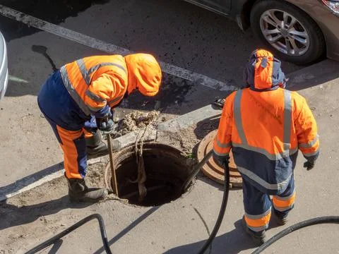 Workers over the open sewer hatch Stock Photos
