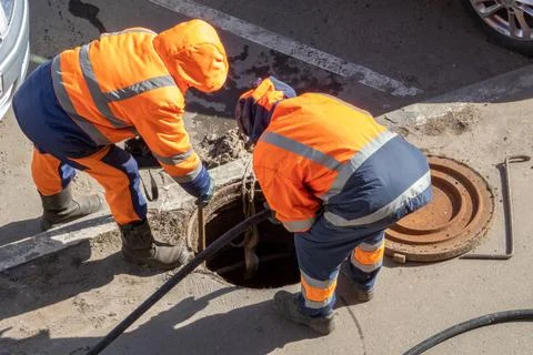 Workers over the open sewer hatch repairing water supply system Stock Photos
