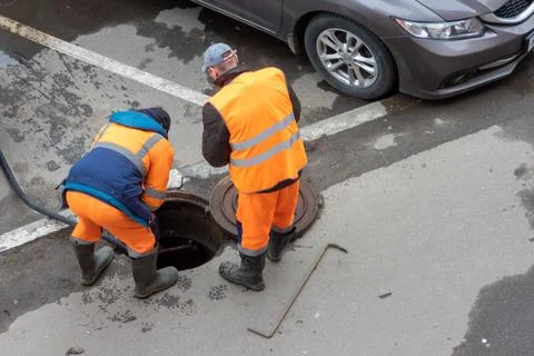 Workers over the open sewer hatch on a street Stock Photos
