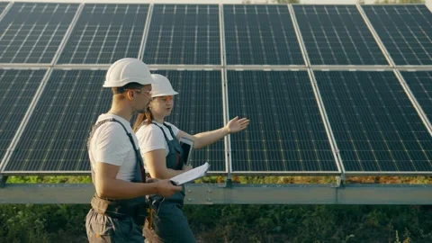 Workers in overalls walk around the solar panel area and analyze data Stock Footage 257133913