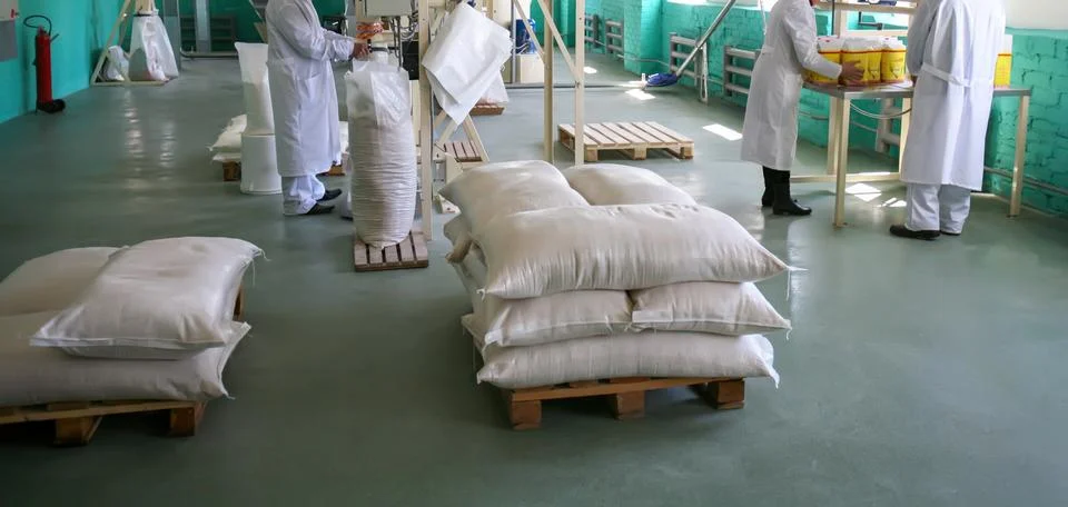 Workers pack and stack bags of grains in a warehouse during the day Stock Photos