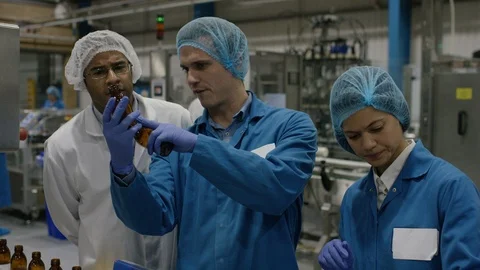 Workers placing inspected bottles on production line in cosmetic factory Stock Footage 107952899