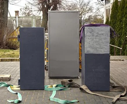 Workers prepare to position large cabinets on a paved area outside a home whi Stock Photos