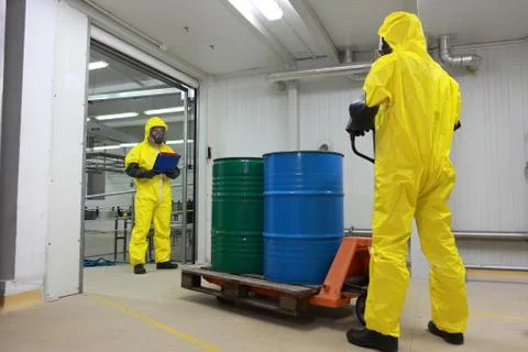 Workers in protective uniforms working with barrels of chemicals on forklift Stock Photos