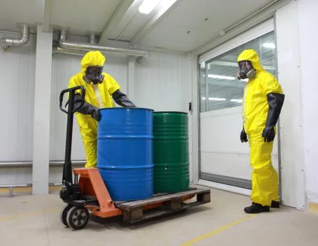 Workers in protective uniforms working with barrels of chemicals on forklift Stock Photos