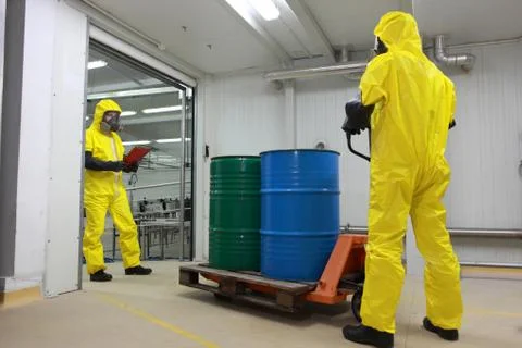 Workers in protective uniforms working with barrels of chemicals on forklift Stock Photos