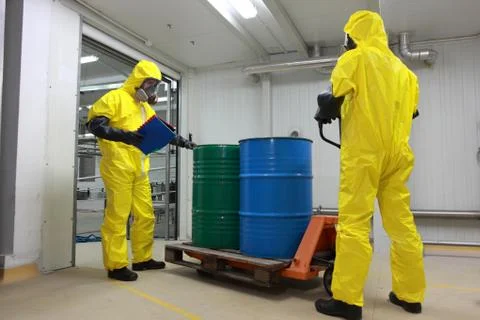 Workers in protective uniforms working with barrels of chemicals on forklift Stock Photos