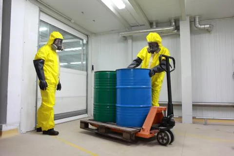 Workers in protective uniforms working with barrels of chemicals on forklift Stock Photos