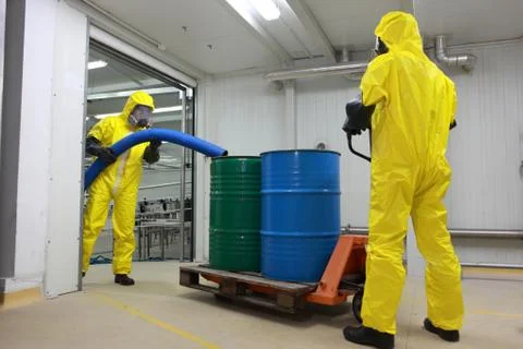 Workers in protective uniforms working with barrels of chemicals on forklift Stock Photos