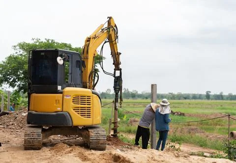 Workers put fence posts into the pit of the excavator. Stock Photos