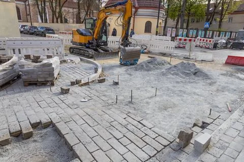 Workers reconstruct a public square using cobblestone paving stones with a ye Stock Photos