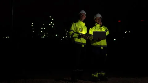 Workers in reflective jackets and helmets are talking to each other at night Video stock 340085001