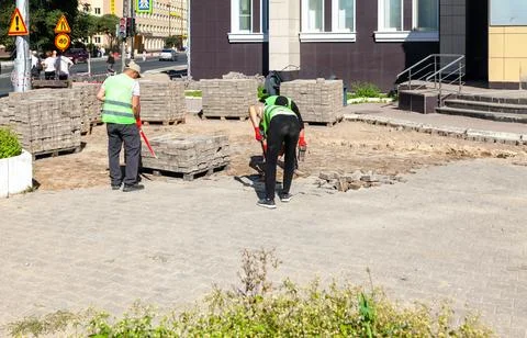 Workers in reflective vests laying paving slabs on city sidewalk Stock Photos