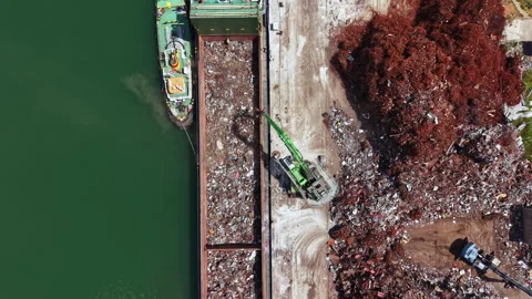 Workers remove waste from a cargo ship at a port in daytime while a crane lifts Stock Footage 337901632