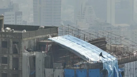 Workers on rooftop spreading blue tarp on unfinished building Video stock 317839995