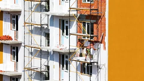 Workers on the scaffolding glues insulation with foam Stock Footage 137086462