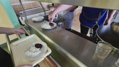 Workers of the school canteen serve schoolchildren by imposing dishes on their Stock Footage 79507997