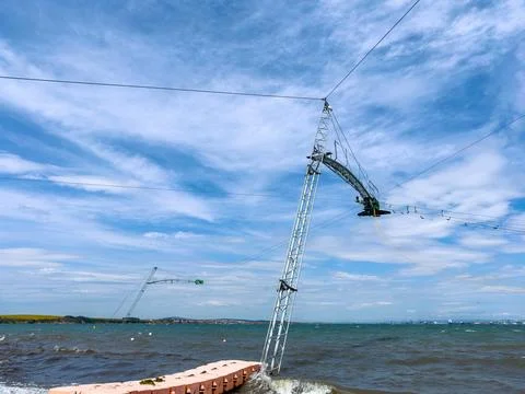 Workers set up a cable system over the water on a sunny day. Waves crash agai Stock Photos