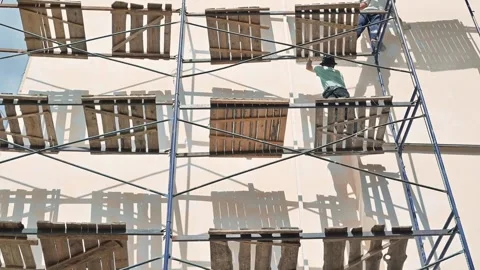 Workers set up scaffolding for a construction project on a building during Stock-Footage 345884223