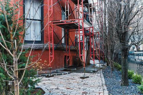 Workers set up scaffolding next to a brick building with trees nearby. The gr 스톡 사진