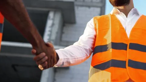 Workers shake hands at a construction site during daylight hours in a city Stock Photos