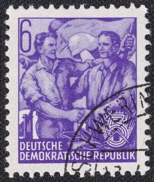 Workers shake hands in front of a flag on a 1957 GDR vintage postage stamp. Stock Photos