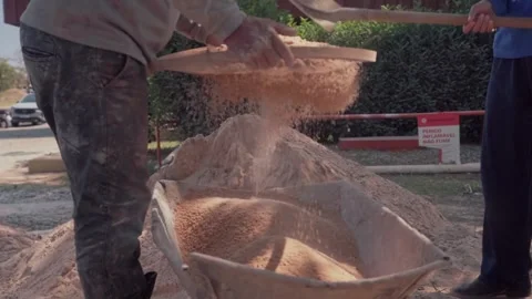 Workers sift sand over a wheelbarrow during construction work in slow motion Video stock 345080029
