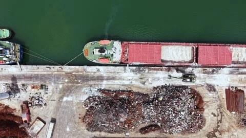 Workers sort and manage scrap metal at a port while a cargo ship is docked Stock Footage 340153452