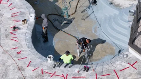 Workers spray pebble sheen finish directly into curved pool basin, hoses plus 動画素材 339097883